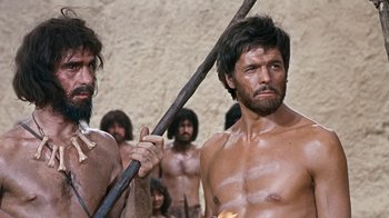 Movie still from “When Dinosaurs Ruled the Earth” (1970), directed by Val Guest – A group of men standing next to each other holding sticks; Medium shot, Low angle