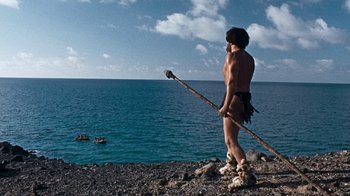 Movie still from “When Dinosaurs Ruled the Earth” (1970), directed by Val Guest – A man standing on the rocks by the water; Wide shot, Low angle