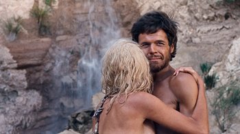 Movie still from “When Dinosaurs Ruled the Earth” (1970), directed by Val Guest – A man and a woman embracing in front of a waterfall; Close Up shot, Overhead angle