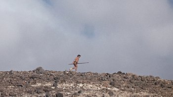Movie still from “When Dinosaurs Ruled the Earth” (1970), directed by Val Guest – A man walking on top of a hill holding a stick; Extreme Wide shot, High angle