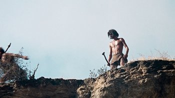 Movie still from “When Dinosaurs Ruled the Earth” (1970), directed by Val Guest – A man that is standing on a hill holding a hammer; Wide shot, Low angle