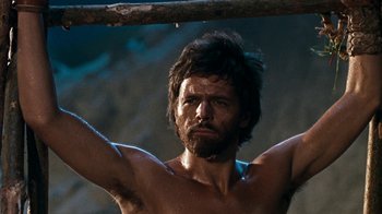 Movie still from “When Dinosaurs Ruled the Earth” (1970), directed by Val Guest – A shirtless man holding onto a wooden stick; Close Up shot, Low angle