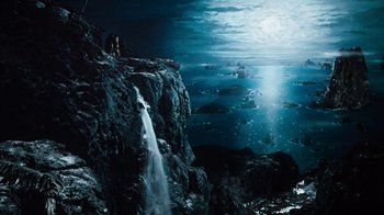 Movie still from “When Dinosaurs Ruled the Earth” (1970), directed by Val Guest – A man standing next to a waterfall in the ocean; Extreme Wide shot, High angle