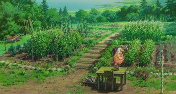 Movie still from “When Marnie Was There” (2014), directed by Hiromasa Yonebayashi – An animated scene of a woman sitting at a table in the middle of a garden; Extreme Wide shot, High angle