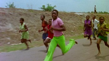 Movie still from “When We Were Kings” (1996), directed by Leon Gast – A group of people running down a street; Medium shot, Low angle