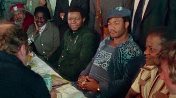 Movie still from “When We Were Kings” (1996), directed by Leon Gast – A group of men sitting around a table; Medium shot, Low angle