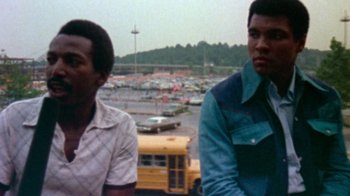 Movie still from “When We Were Kings” (1996), directed by Leon Gast – Two men standing next to each other in a parking lot; Medium shot, Low angle
