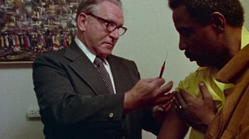 Movie still from “When We Were Kings” (1996), directed by Leon Gast – An older man in a business suit is holding a needle in his hand; Medium shot, Low angle