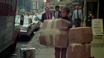 Movie still from “When We Were Kings” (1996), directed by Leon Gast – A woman carrying a large box down a street; Wide shot, High angle