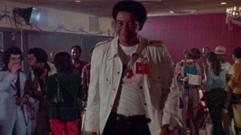 Movie still from “When We Were Kings” (1996), directed by Leon Gast – A man in a white jacket is standing in front of a group of people; Medium shot, Low angle