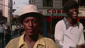 Movie still from “When We Were Kings” (1996), directed by Leon Gast – A man wearing a hat standing in front of a building; Medium shot, Low angle