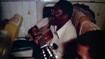 Movie still from “When We Were Kings” (1996), directed by Leon Gast – A man sitting down playing an instrument; Close Up shot, High angle