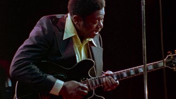 Movie still from “When We Were Kings” (1996), directed by Leon Gast – A man playing a guitar on a stage; Close Up shot, Low angle