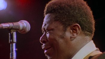 Movie still from “When We Were Kings” (1996), directed by Leon Gast – A person singing on a microphone; Close Up shot, Low angle