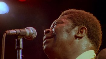 Movie still from “When We Were Kings” (1996), directed by Leon Gast – A person singing on a microphone; Extreme Close Up shot, Low angle
