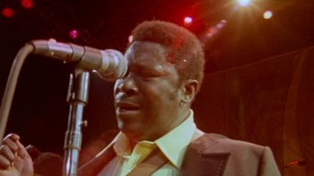 Movie still from “When We Were Kings” (1996), directed by Leon Gast – A person on a stage with a microphone; Close Up shot, Low angle