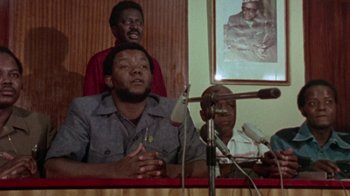 Movie still from “When We Were Kings” (1996), directed by Leon Gast – A man sitting in front of microphones at a press conference; Medium shot, Low angle