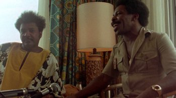 Movie still from “When We Were Kings” (1996), directed by Leon Gast – A man and a woman sitting at a table talking to each other; Medium shot, Over the shoulder angle