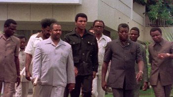 Movie still from “When We Were Kings” (1996), directed by Leon Gast – A group of men standing next to each other in front of a building; Medium shot, Low angle