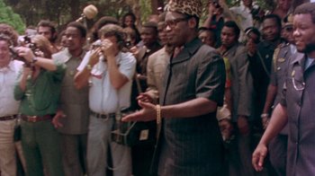 Movie still from “When We Were Kings” (1996), directed by Leon Gast – A man standing in front of a group of people; Medium shot, Over the shoulder angle