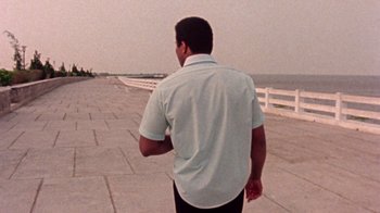 Movie still from “When We Were Kings” (1996), directed by Leon Gast – A man walking on a sidewalk near the ocean; Medium shot, Low angle