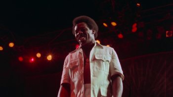 Movie still from “When We Were Kings” (1996), directed by Leon Gast – A man standing on a stage in front of a crowd; Medium shot, Low angle