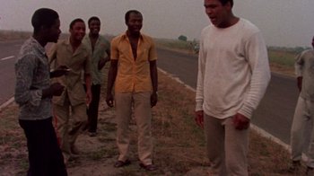 Movie still from “When We Were Kings” (1996), directed by Leon Gast – A group of men standing next to each other on the side of a road; Medium shot, Low angle