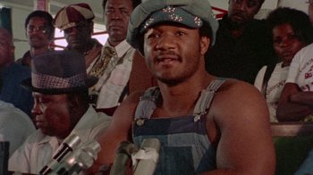 Movie still from “When We Were Kings” (1996), directed by Leon Gast – A man with a hat on sitting next to other men; Close Up shot, Low angle