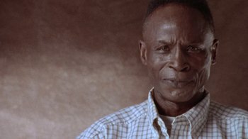 Movie still from “When We Were Kings” (1996), directed by Leon Gast – An older man wearing a checkered button up shirt; Close Up shot, Low angle