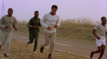 Movie still from “When We Were Kings” (1996), directed by Leon Gast – Two men running on the side of a road; Medium shot, Low angle