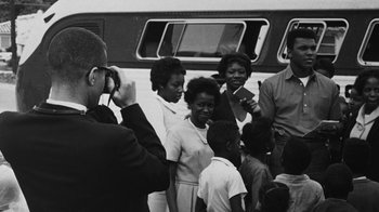 Movie still from “When We Were Kings” (1996), directed by Leon Gast – A group of people standing next to each other near a bus; Medium shot, Over the shoulder angle