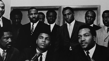 Movie still from “When We Were Kings” (1996), directed by Leon Gast – A black and white photo of a group of men in suits and ties; Extreme Close Up shot, Low angle