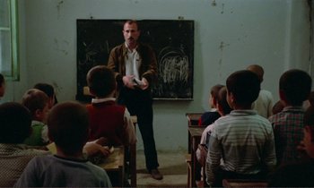 Movie still from “Where Is the Friend's House?” (1987), directed by Abbas Kiarostami – A man standing in front of a group of people; Wide shot, Over the shoulder angle