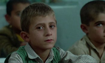 Movie still from “Where Is the Friend's House?” (1987), directed by Abbas Kiarostami – A young boy sitting in front of other boys; Close Up shot, Over the shoulder angle