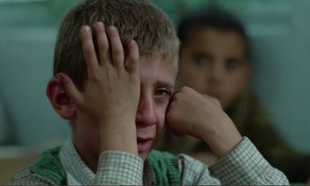 Movie still from “Where Is the Friend's House?” (1987), directed by Abbas Kiarostami – A young boy holding his hand up to his face; Close Up shot, Over the shoulder angle
