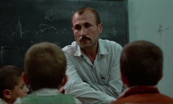 Movie still from “Where Is the Friend's House?” (1987), directed by Abbas Kiarostami – A man sitting in front of a group of children; Close Up shot, Over the shoulder angle