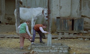 Movie still from “Where Is the Friend's House?” (1987), directed by Abbas Kiarostami – Two young boys and a white horse standing next to each other; Wide shot, High angle