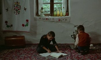 Movie still from “Where Is the Friend's House?” (1987), directed by Abbas Kiarostami – Two young children are sitting on the floor reading a book; Wide shot, High angle