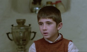 Movie still from “Where Is the Friend's House?” (1987), directed by Abbas Kiarostami – A young boy wearing a red vest looking at the camera; Close Up shot, Over the shoulder angle