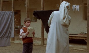 Movie still from “Where Is the Friend's House?” (1987), directed by Abbas Kiarostami – A young boy reading a book to an older man; Medium shot, Over the shoulder angle