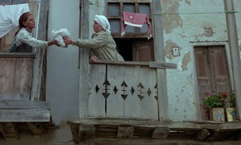 Movie still from “Where Is the Friend's House?” (1987), directed by Abbas Kiarostami – An old woman is reaching out of a window to grab a stuffed animal; Wide shot, Low angle