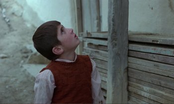 Movie still from “Where Is the Friend's House?” (1987), directed by Abbas Kiarostami – A young boy looking up into the sky; Medium shot, Low angle
