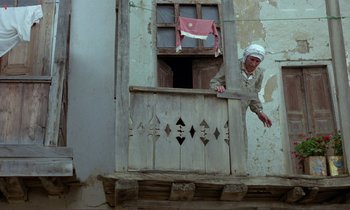 Movie still from “Where Is the Friend's House?” (1987), directed by Abbas Kiarostami – An old man standing on the balcony of an old building; Wide shot, Low angle