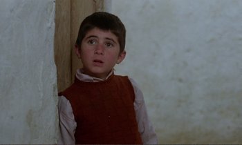 Movie still from “Where Is the Friend's House?” (1987), directed by Abbas Kiarostami – A young boy wearing a red vest looking up at the sky; Close Up shot, High angle