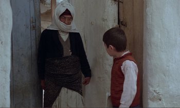Movie still from “Where Is the Friend's House?” (1987), directed by Abbas Kiarostami – A man and a boy are standing next to each other; Medium shot, Over the shoulder angle