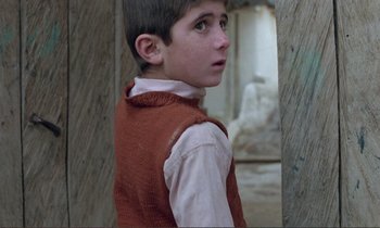 Movie still from “Where Is the Friend's House?” (1987), directed by Abbas Kiarostami – A young boy wearing a red vest looking up; Close Up shot, Over the shoulder angle