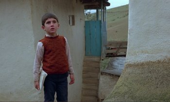 Movie still from “Where Is the Friend's House?” (1987), directed by Abbas Kiarostami – A young boy standing in front of a building; Medium shot, Low angle