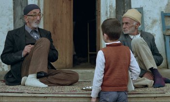 Movie still from “Where Is the Friend's House?” (1987), directed by Abbas Kiarostami – A group of men sitting on the ground talking to each other; Wide shot, Over the shoulder angle