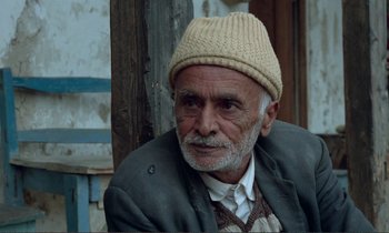 Movie still from “Where Is the Friend's House?” (1987), directed by Abbas Kiarostami – An old man wearing a white hat and a jacket; Medium shot, Low angle