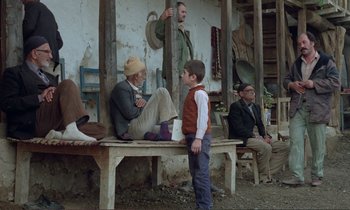 Movie still from “Where Is the Friend's House?” (1987), directed by Abbas Kiarostami – A group of people sitting on a bench; Wide shot, Over the shoulder angle